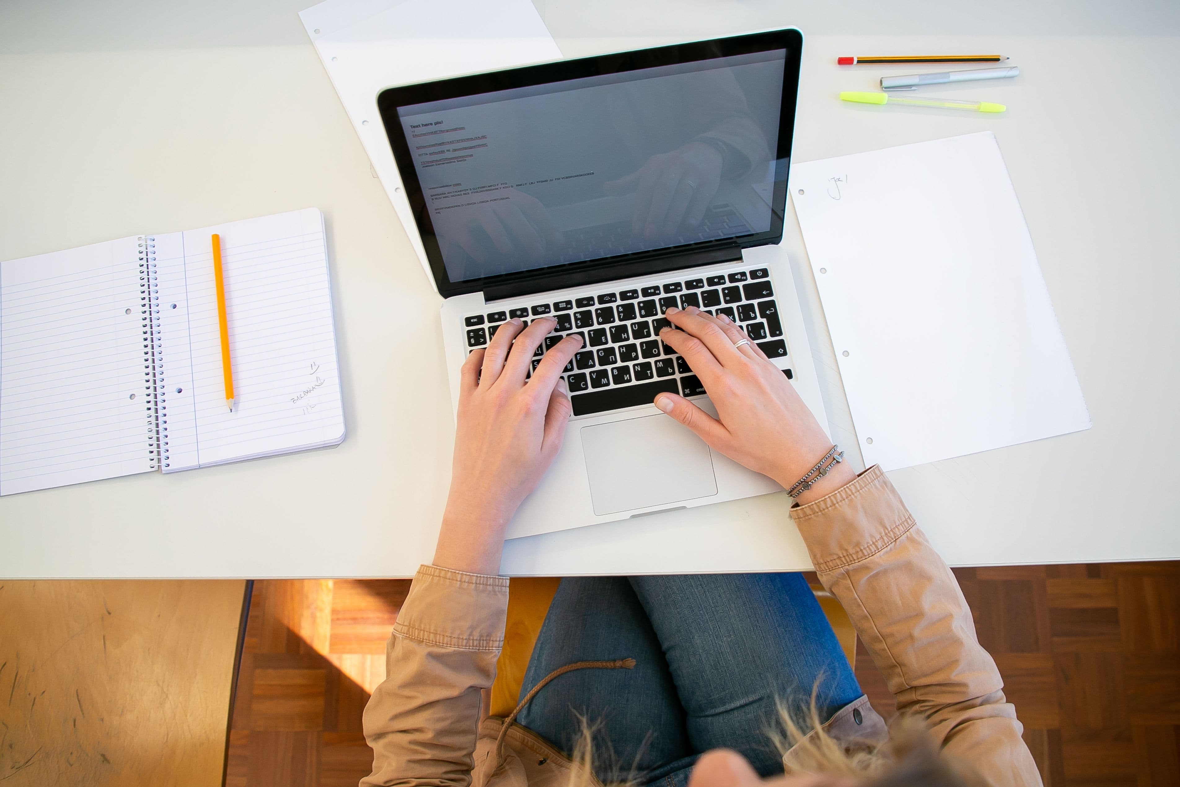 The image shows an overhead photo of a student working on a laptop with papers and notes around them.